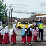 Seorang Polwan Polres Blora membantu siswa SD menyeberang jalan di depan SD Negeri Tempelan, Blora, Jumat (7/11/2025).