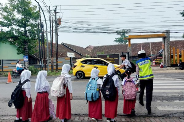 Seorang Polwan Polres Blora membantu siswa SD menyeberang jalan di depan SD Negeri Tempelan, Blora, Jumat (7/11/2025).